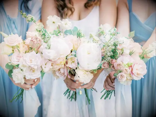 A bride and her bridesmaids hold pale white, pink, and yellow flowers.