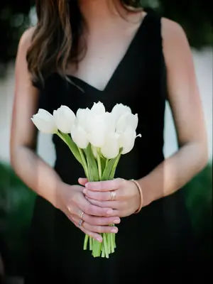 A bridesmaid holds a bouquet of white tulips.
