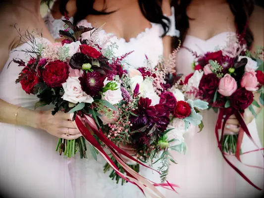 Bridesmaids hold vibrant wine-toned and pink bouquets.