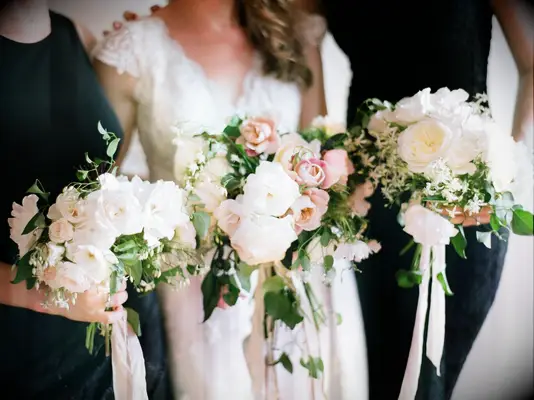 A bride and her bridesmaids hold white and pale pink bouquets.