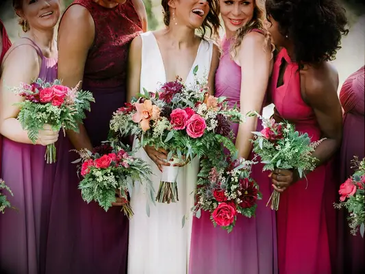 a bride stands with her bridesmaids carrying fall bouquets with fuchsia and orange flowers