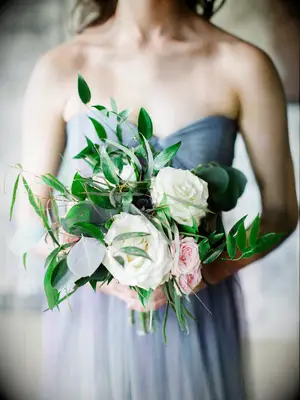 A bridesmaid holds a bouquet of roses and vibrant greenery.