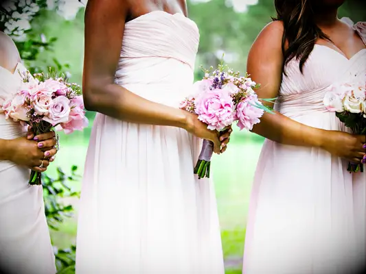 Bridesmaids hold pale pink bouquets.