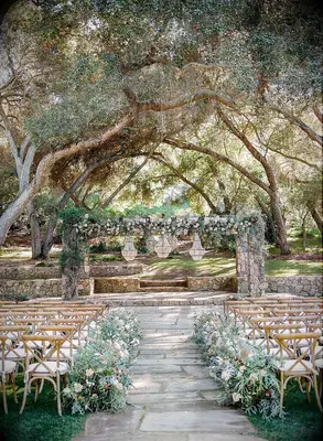 Rustic outdoor wedding ceremony with cross-back chairs and stone arch