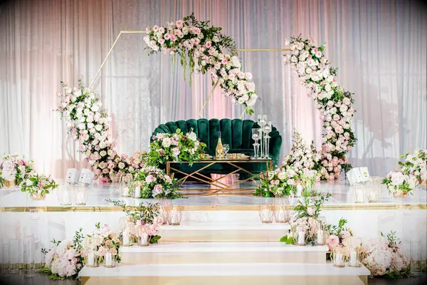 Sweetheart table on stage with emerald velvet couch and gold hexagon arch backdrop