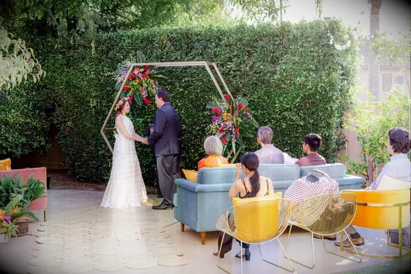 Couple exchanging vows in backyard in front of gold hexagon arch