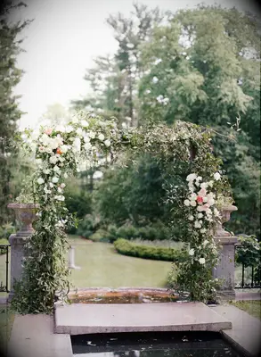 Ceremony arch in garden covered in greenery and white roses
