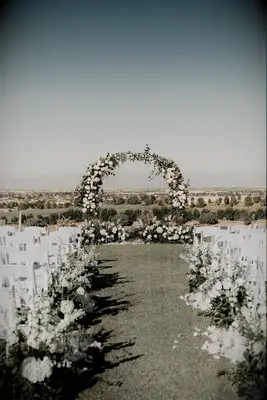 Outdoor ceremony with white chairs and flower-covered circle arch