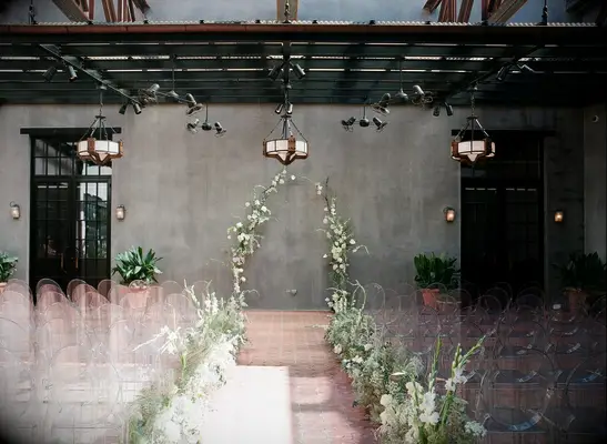 Ceremony on hotel patio with greenery arch and ghost chairs