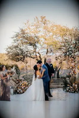 Couple kissing during outdoor ceremony in front of copper arch