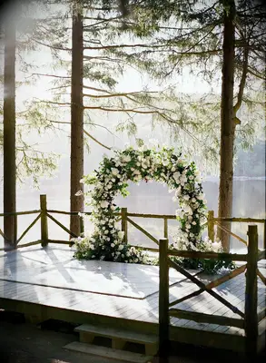 Arch covered in white flowers overlooking woodsy lake