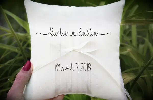 White ring bearer pillow with personalized couples name in black text