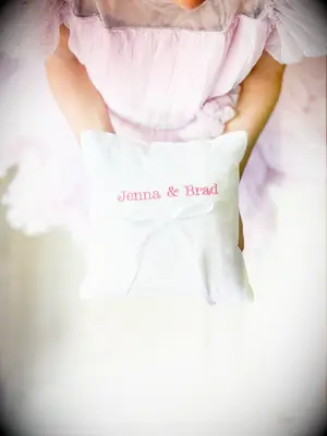 White linen ring bearer pillow with pink embroidered couples name