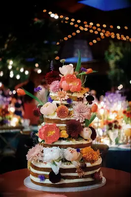 Exposed tiered wedding cake with colorful florals and fruit