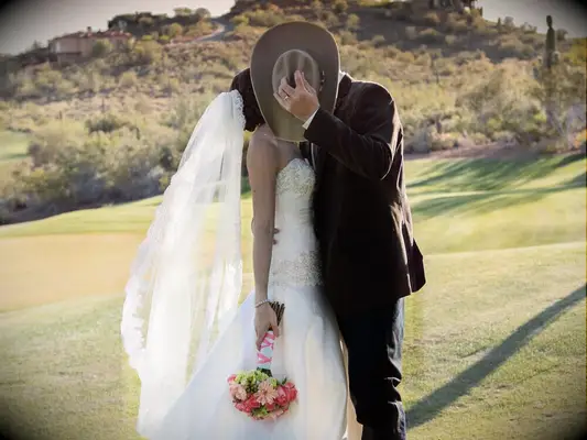 Bride and groom kissing behind a cowboy hat. 