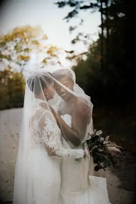 Brides holding each other under a large veil. 