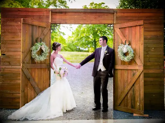Bride and groom standing in front of a barn doorway.