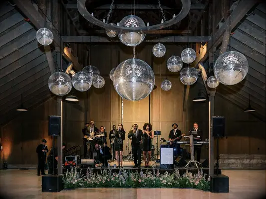 Wedding band performing in a barn with multiple disco balls above them. 