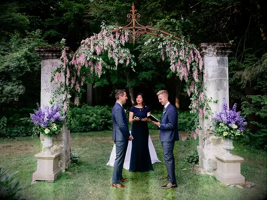 Grooms exchanging vows at outdoor whimsical garden wedding venue with hanging wisteria