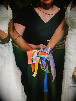 Brides holding hands during colorful ribbon binding unity ceremony