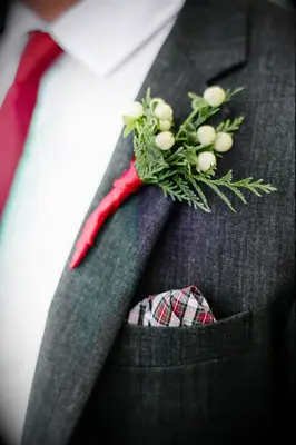 close up of winter wedding boutonniere with white berries, evergreens, red plaid pocket square and matching red tie
