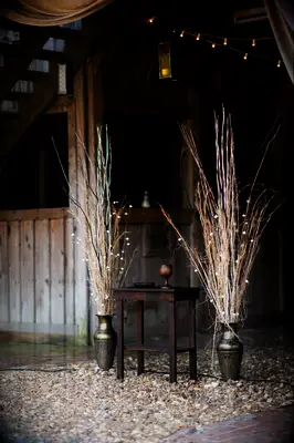 wedding altar decor with tall branches and string lights in bronze urns at rustic barn venue