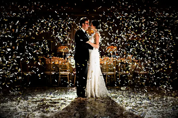 bride and groom standing in the middle of the dance floor with white and gold confetti falling around them
