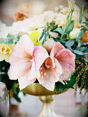 A flower arrangement in a gold vessel with pink amaryllis flowers