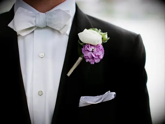 A boutonniere with a purple camellia flower on a tuxedo lapel