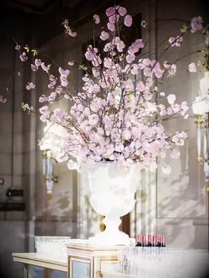 A white urn flower arrangement with flowering cherry blossom branches