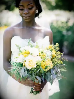 A bride holding a yellow bouquet of craspedia and goldenrod flowers
