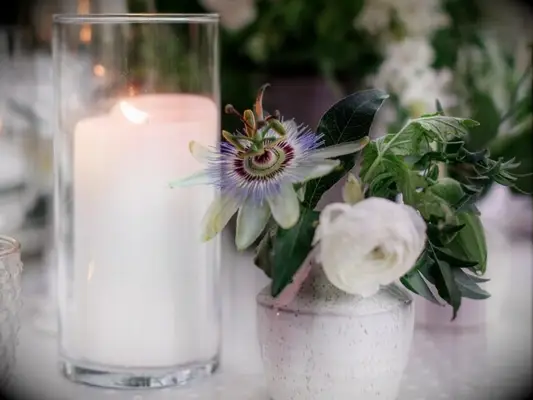 A bud vase with ranunculus and passionflower blooms beside pillar candle