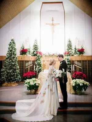 Couple standing at church altar surrounded by poinsettia plants