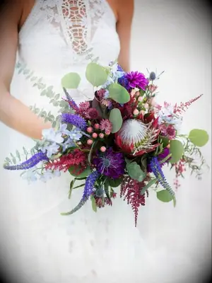 Bride holding purple bouquet with veronica and protea