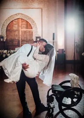 Groom lifting his bride out of her wheelchair