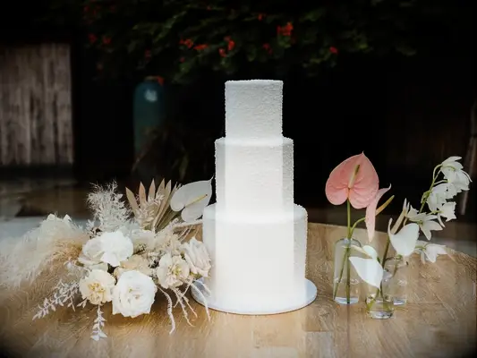 white wedding cake beside boho anthurium flower arrangement