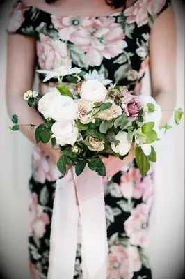 bridesmaid wearing black and pink floral print dress holding small bouquet of blush roses, white ranunculus and greenery