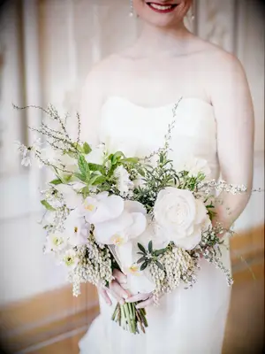 bride holding elegant spring wedding bouquet with white orchids, roses and pieris japonica