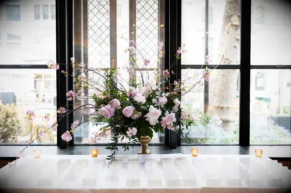 wedding escort table decorated with a centerpiece of pink cherry blossom branches and pink peonies