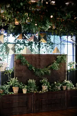 wedding DJ booth decorated with greenery garland and white potted plants in terracotta pots