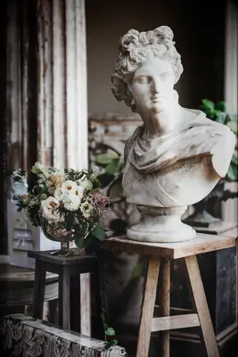 roman goddess statue on a wooden stool next to small white and blush wedding centerpiece