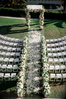 aerial view of outdoor wedding ceremony aisle lined with white flower arrangements along the side and flower petals scattered down the aisle