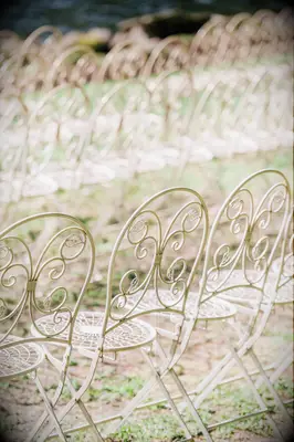 rows of white vintage wrought iron folding chairs on the grass at outdoor wedding ceremony