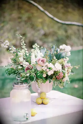 self serve wedding drink station with lemonade in glass beverage dispenser next to pastel pink floral centerpiece