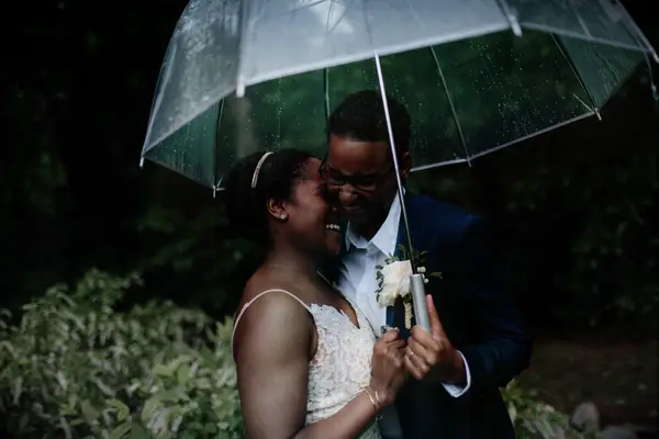 same sex couple two brides laughing and hugging under an umbrella at outdoor spring wedding