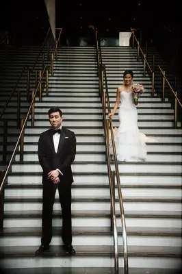 bride walks down the stairs at san francisco city hall to surprise groom with his back turned