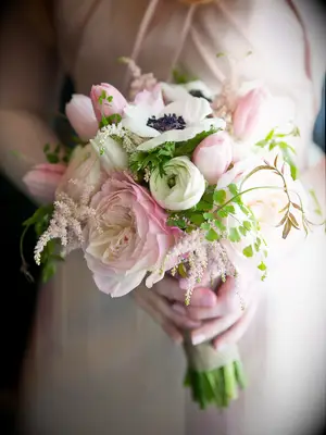 A bride holds a bouquet of pale pink roses and white and black panda anemones.