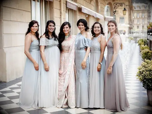 A bride poses with her wedding party, who all appear in dresses with pale pastel shades.