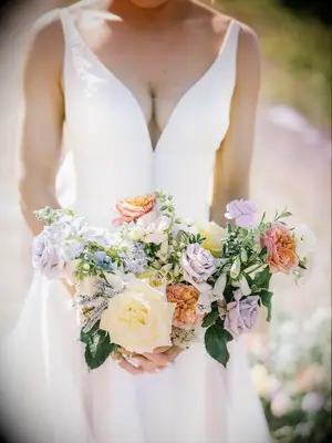 A bride carries a spring-toned bouquet in pale lavendar, yellow, peach and sky blue.