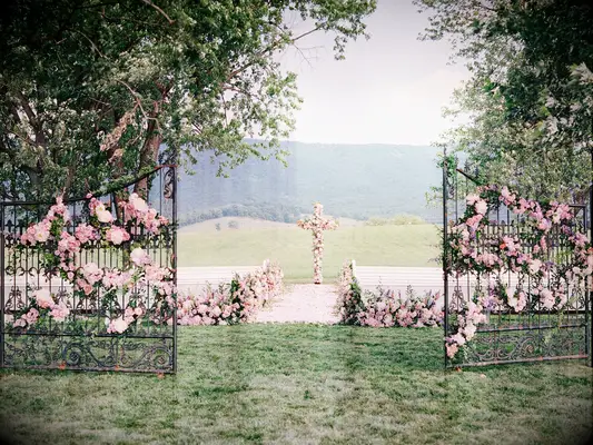 outdoor wedding ceremony venue with iron gates and cross decorated in pink roses